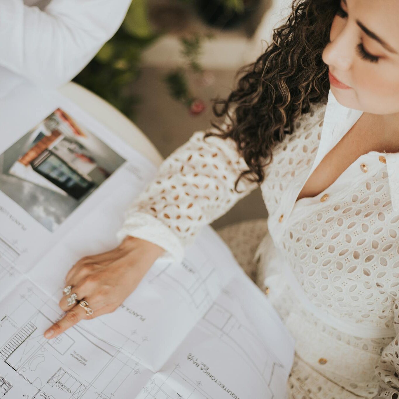 A woman reviews architectural floor plans on a table with a tablet in a modern workspace.