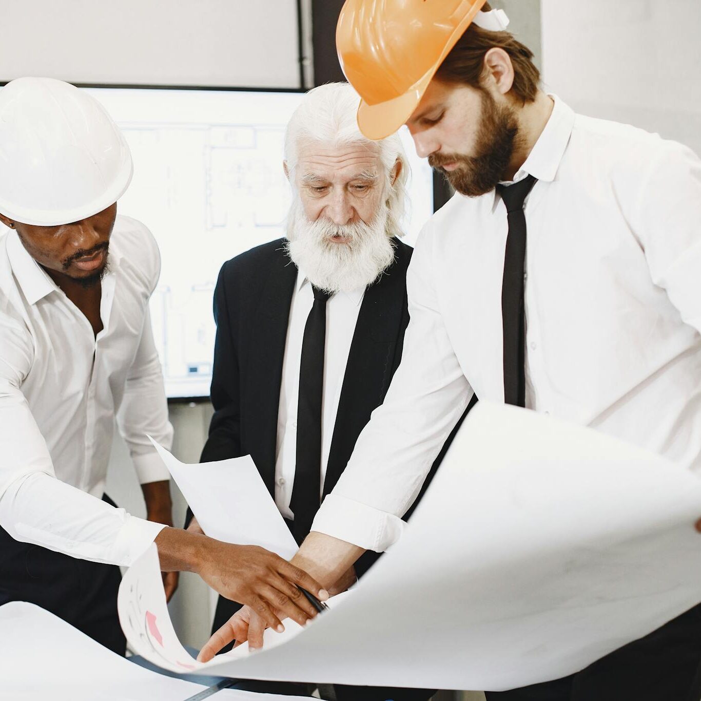 Three architects in office reviewing blueprints, showcasing teamwork and professional attire.